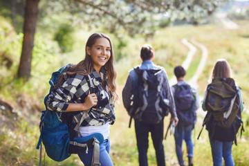 Girl with a backpack with friends, tourists walking in nature. - obrazy, fototapety, plakaty