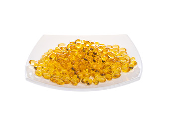 Softgels of Omega-3 on a white plate. Vitamins fish oil on a white background. Yellow capsules with medicine. Meal replacement. Medical medicament of polyunsaturated fatty acids. Open aperture
