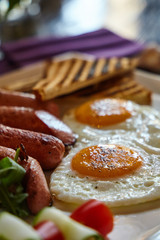 Breakfast meal composition closeup picture - fried eggs, sausages and vegetables. Blurry food and drinks colorful background