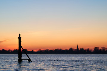 dolphin structure in the river Weser in front of the silhouette of the church St. Laurentius in...