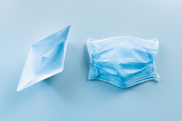 Obraz premium Vacanze a mare ai tempi del Coronavirus. Concetto con barchetta di carta e mascherina chirurgica.