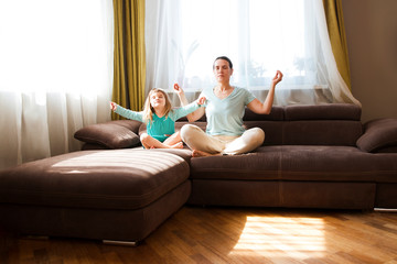 mom with child daughter doing yoga exercise at home. little girl sitting in lotus pose on couch together. Living with a child in quarantine. stay home concept