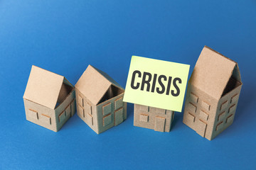 Cardboard toy houses on blue background with crisis sign. Falling property prices. Economic...