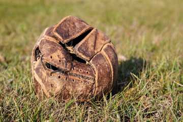 Old leather ball in poor condition on an abandoned football field.