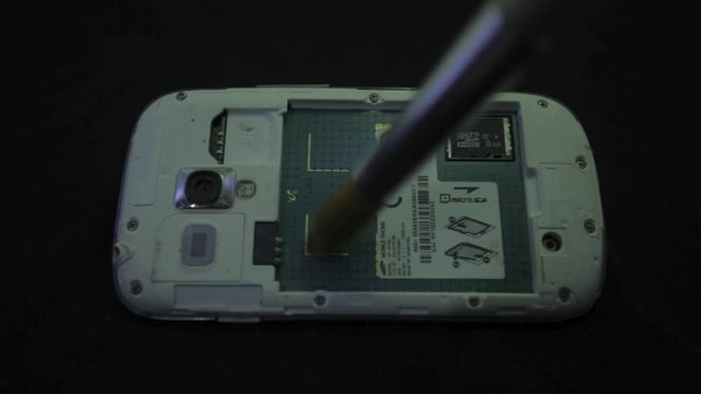 Using a small brush to clean the dust off the back of a mobile phone - close up
