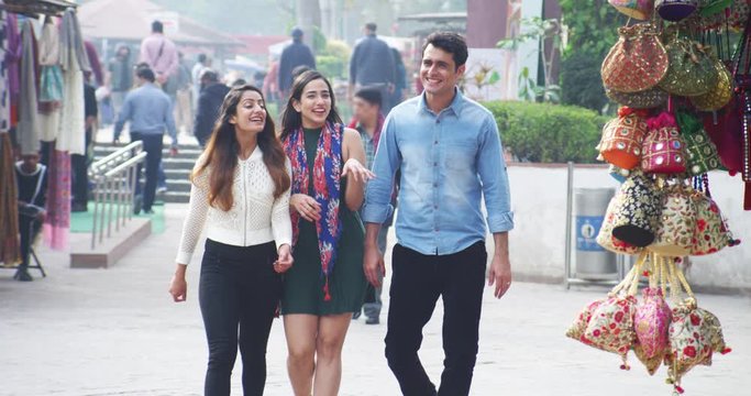 4K Happy Indian male & female friends walking through busy city market, chatting & laughing. Slow motion.