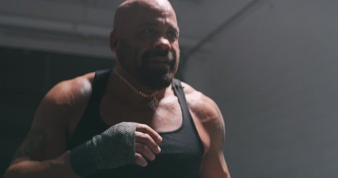 Low angle of bald, tan, muscular boxer training.