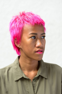 Face of young rebellious Asian woman with pink hair thinking