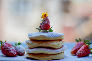 Stack of delicious fluffy pancakes with fresh strawberries and sugar and honey