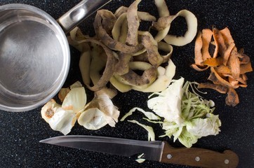 Top view of leftover vegetable peelings, knife and pot on the black kithcen table