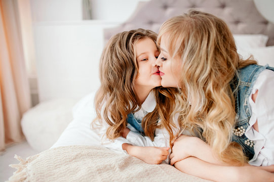 Have a good time at home. Mom kisses daughter on the bed in the bedroom.