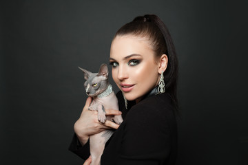 Glamorous woman in diamond earrings with sphynx cat on black background