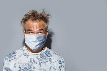 Funny mature man with messy hair wearing protective mask over light background
