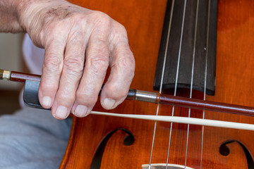 Hand eines alten Mannes hält Bogen eines Cellos