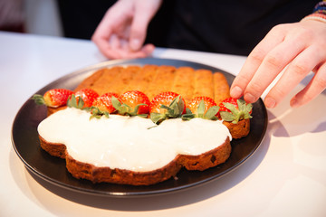 Delicious carrot cake in sour cream sauce with fresh strawberries served on the black serving plate