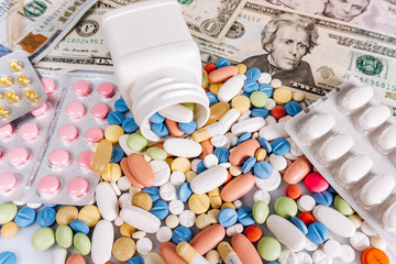 a lot of medical pills in different colors and capsules on a dollar bills, view from above