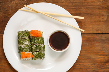 A set of rolls with dill and salmon on a plate with soy sauce and chopsticks.