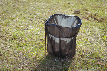 Waste bag with a picnic holder. Disposable black garbage bag on a grass background. Temporary trash...
