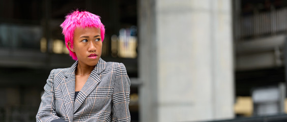 Young rebellious Asian businesswoman with pink hair thinking outdoors