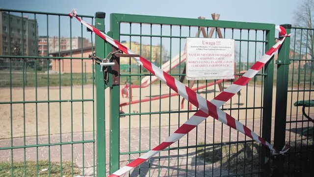 White and red tape prohibiting anyone from entering the playground. Place closed until further notice. The gate is locked with a padlock. Time coronavirus epidemic in Europe