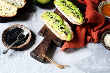 Sandwich with avocado, curd cheese, chia seeds and sesame seeds on a gray background