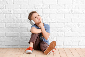 Cute little boy listening to music near white brick wall