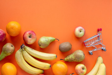 Fruits and small shopping card on a orange background top view