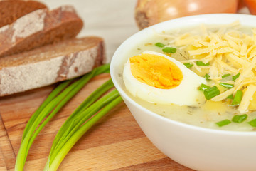 White plate of cheese and potato onion soup with grated cheese sprinkled on top and half a boiled egg close-up.