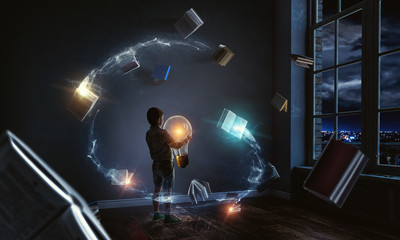 Fototapeta na wymiar Boy holding a light bulb with books around him