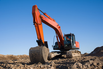 Excavator during earthmoving work at open-pit mining on blue sky background. Loader machine with...