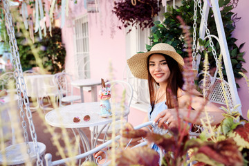 Good-looking woman wearing wide-brim hat is sitting outdoors in the street cafe. Summertime. 