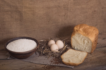A cut piece of white bread, eggs and flour on a wooden table