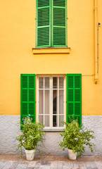 Fototapeta na wymiar Green wooden shutters on yellow wall by a narrow street in Alcudia, Mallorca, Spain.
