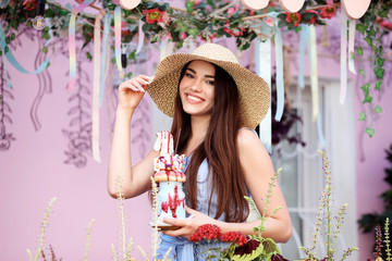 Pretty long haired girl in the wide-brim hat is smiling and holding a moilkshake in her hand. 