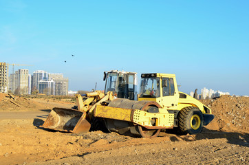 Soil Compactor and  wheel loader at construction site. Vibration single-cylinder road roller leveling the ground for the construct of the foundation for residential building, office, shopping center.