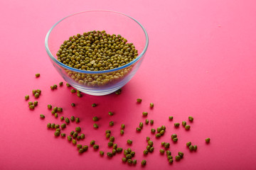 Glass jar with green cereal mung bean on a pink background.