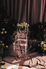 transparent chair in a wedding decor, lit by lateral sunlight, around flowers and rose leaves