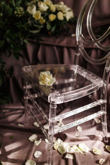 transparent chair in a wedding decor, lit by lateral sunlight, around flowers and rose leaves
