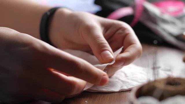 Young tailor attaches white textile pieces with sewing pins making reusable face mask at workplace night at home. Female hand taking pins from the brown ball of thread. Close up