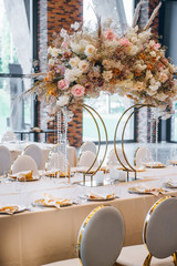 A large floral arrangement of an unusual shape stands on a beautiful festive table on the wedding