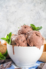 Homemade chocolate ice cream with chocolate pieces and shavings, and ice cream cones. In small white bowls on white grey stone table copy space