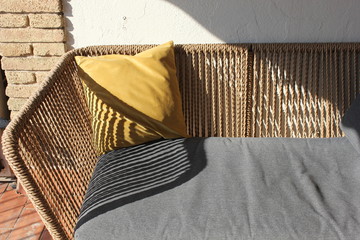 brown rattan terrace sofa with gray mattress and yellow pillow and stripes of shade from the sun rays