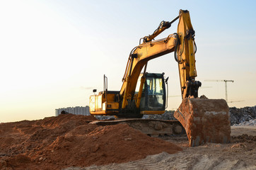 Excavator at construction site on sunset background. Earth-moving heavy equipment for digg ground, foundation and trenchs for laying sewer pipes and water main reticulation systems.