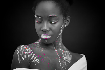 african woman with body art glowing in ultraviolet light. Portrait of beautiful woman painted in fluorescent powder. isolated dark space. black and white photo