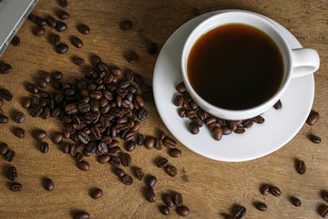 White coffee cup and coffee beans on wooden table with copyspace for text. Selective focus.