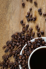 White coffee cup and coffee beans on wooden table with copyspace for text. Selective focus.