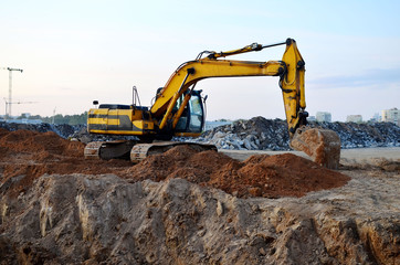 Excavator with a large iron bucket on a construction site during road works. Backhoe dig the ground for the foundation, laying storm sewer pipes. Installation of water main systems.