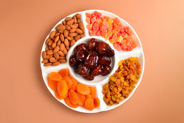 Mix of dried fruits and nuts on a white plate. Apricot, almond, raisin, dates fruit. On a brown background. Space for text or design.