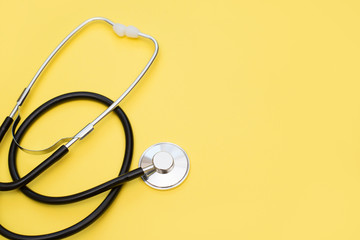 Above shot of a stethoscope puts on the left side of a yellow background with a copy space