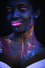 unusual interesting shoot of young african woman with fluorescent make-up on face, fluorescent prints glows on neon lights, ultra-violet. body art concept